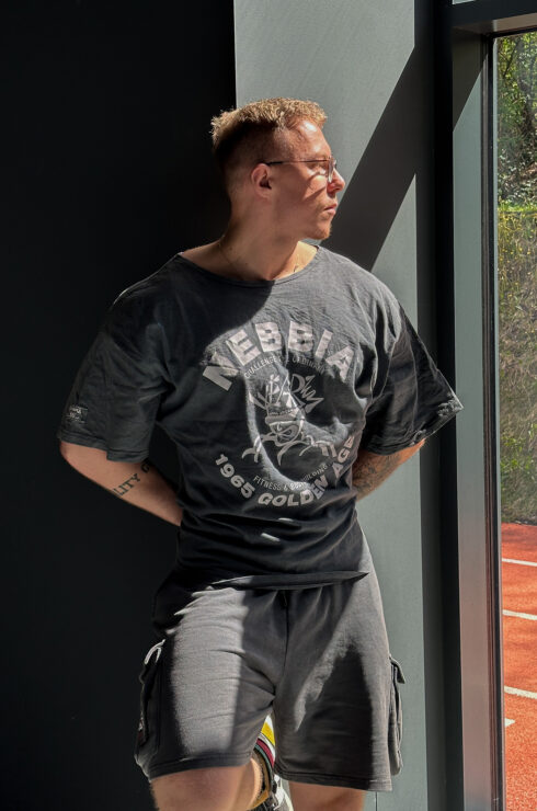 Washed-off efekt, cargo detaily a bodybuilding DNA. Pocta časom, keď sa budovali legendy bez skratiek a filtrov. Ján Potočár si vybral: Toto vôbec nie je hocijaké tričko — je to kúsok pre lifterov, ktorí chcú ukázať svoje tvrdo vydreté gains! Pritom nezabúdajú vzdať hold zlatej ére kulturistiky, ku ktorej všetci vzhliadame. Rag top strih je top voľba, pretože je voľný, ale zároveň zdôrazňuje to, čo má: Zvýrazní ramená, hruď, bicepsy, takže tvoj progres bude fakt neprehliadnuteľný. Vypratý washed-off efekt má ten správny old-school vibe. S výrazným NEBBIA a Mr. Olympia brandingom a grafikou Golden Age 1965, sú bodybuilderské legendy v gyme s tebou. Či už makáš v posilke alebo vyrazíš do ulíc, v tomto tričku zostávaš verný pravému odkazu kulturistiky. Vytvorené pre gym bros, ktorý si idú za svojim a neboja sa challengeovať svoj výkon každý deň! Teplákové šortky spájajú drsný bodybuilderský štýl a maximálny komfort. A ani náhodou to nie sú to len ďalšie trendy cargo kraťasy — sú vytvorené pri príležitosti 60-ročného odkazu Mr. Olympia a ak ťa už toto nenakopne k novému PR, tak potom čo? Voľný strih ti poskytne maximálnu slobodu pohybu a washed-off efekt dodáva šortkám drsný old-school vibe. S praktickými cargo vreckami máš všetko potrebné vždy poruke, takže sa môžeš plne sústrediť na svoj tréning. Výrazné logo NEBBIA spolu s Mr. Olympia brandingom na vreckách vyjadrujú poctu fitnessu a najslávnejšej ére bodybuildingu!